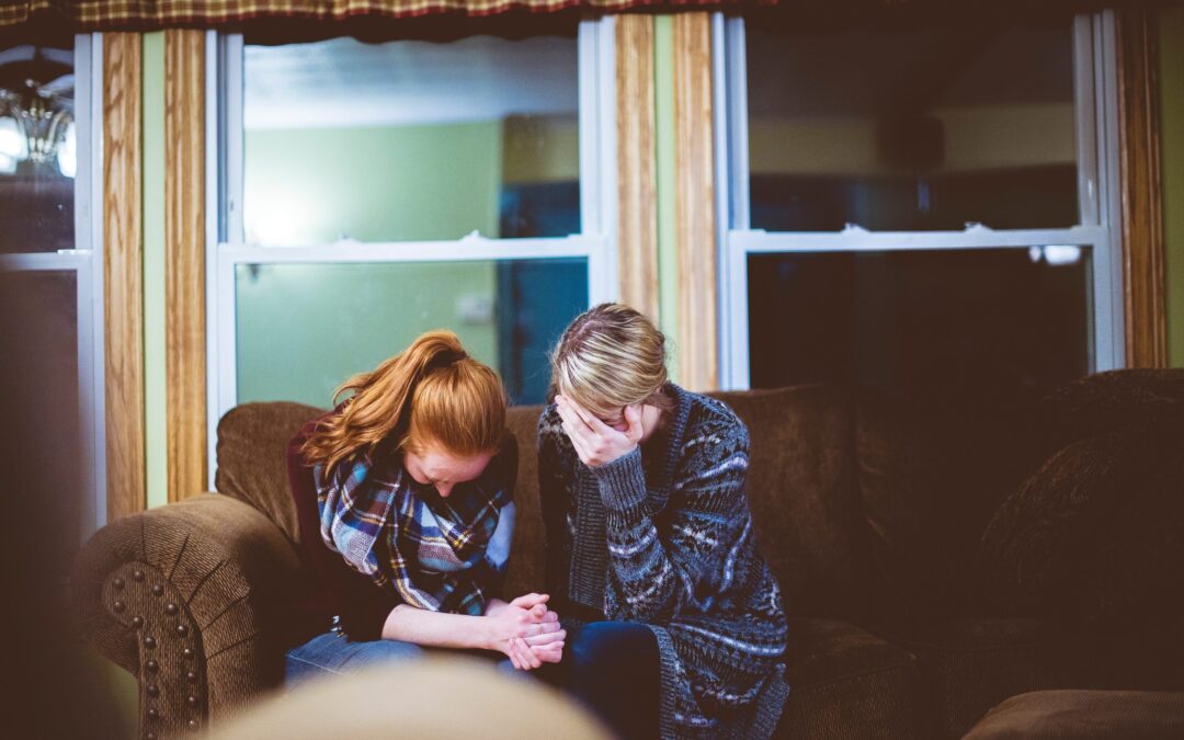 two woman share a moment together with heads bowed and clasping hands.