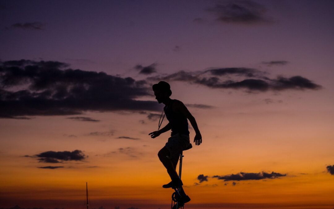 nitetime, a man wearing a hat and tshirt rides a unicycle that is very tall.