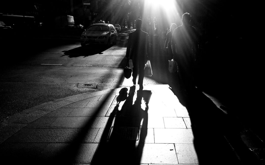 a group of people walk in the daylight on a street, the sun flare is right on top of them in a black and white image.