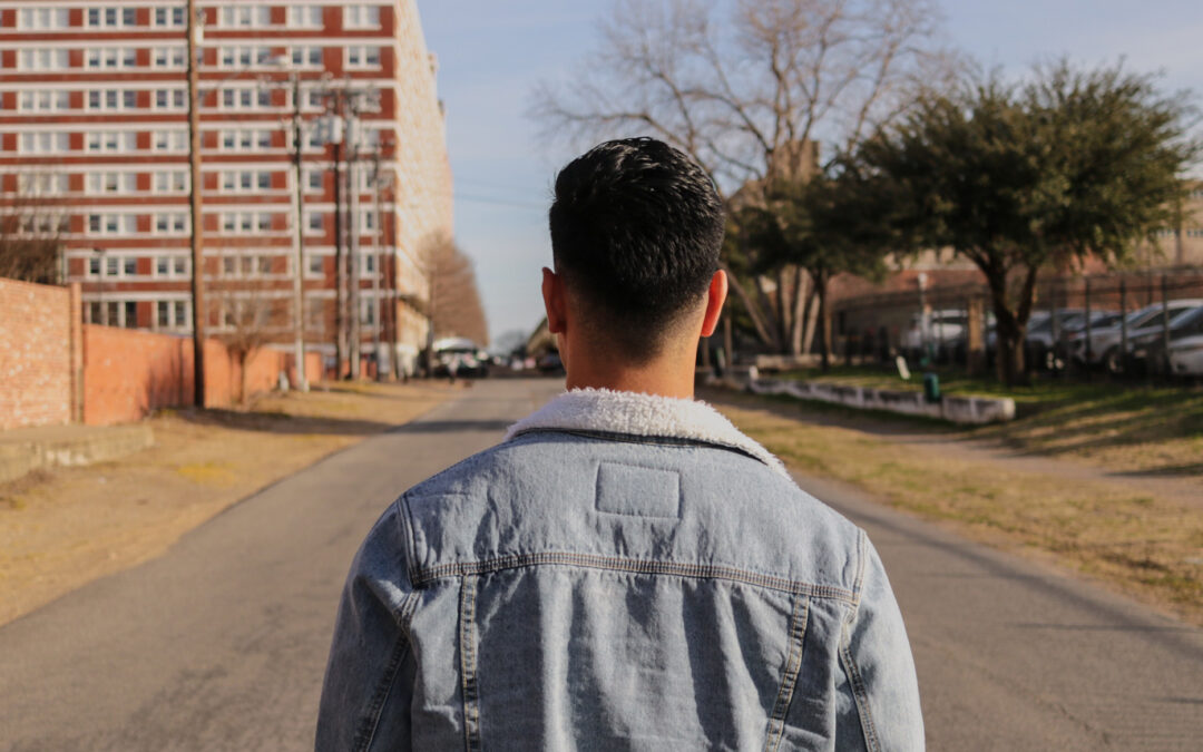 a man walks towards an apartment complex on a rural street.