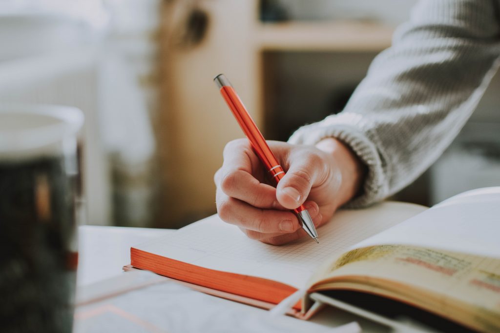 close up of a hand holding a pencil writing on a journal book