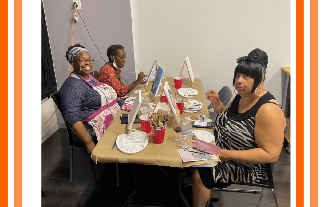 3 women are painting on canvas on a large table.