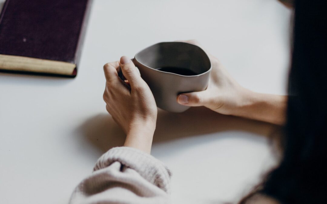 a woman holding a coffee mug talking to another person across from her at a table.