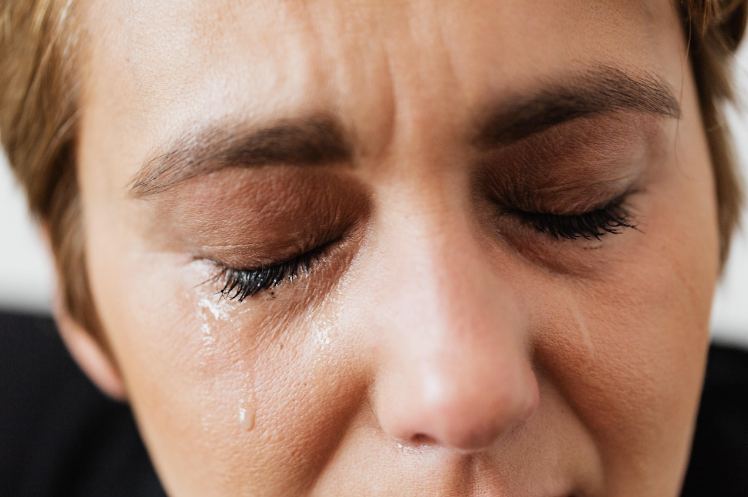 a woman crying with her eyes shut and tears streaming down her face.