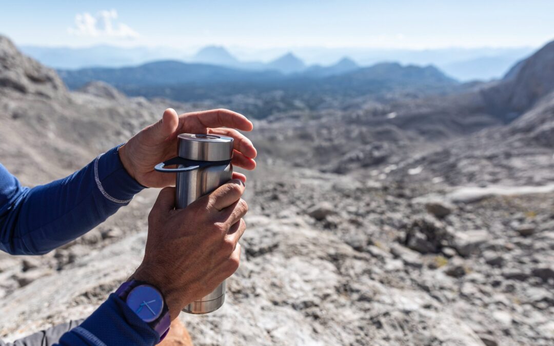 Person holding a stainless steel cup on a mountain trail.