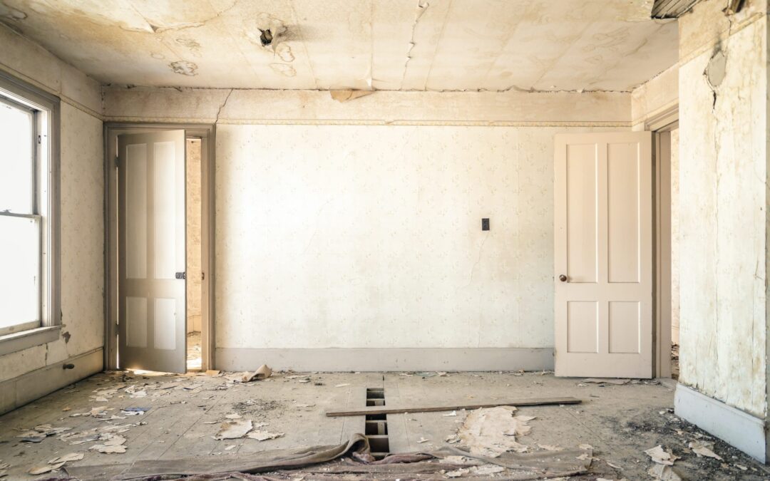 the interior of a house or apartment, the room has heavy water damage, and floor board is ripped up. While the room is empty of everything except debris the room is in a very bad state.