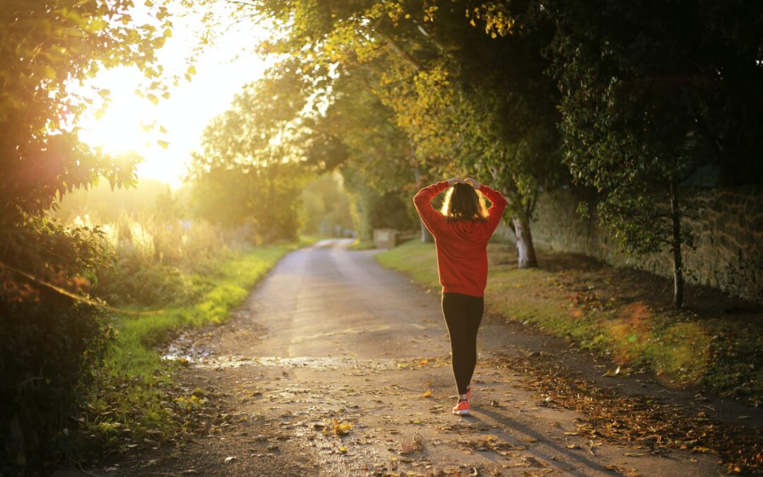 A woman walking in a trail with trees and a brick wall on the right.