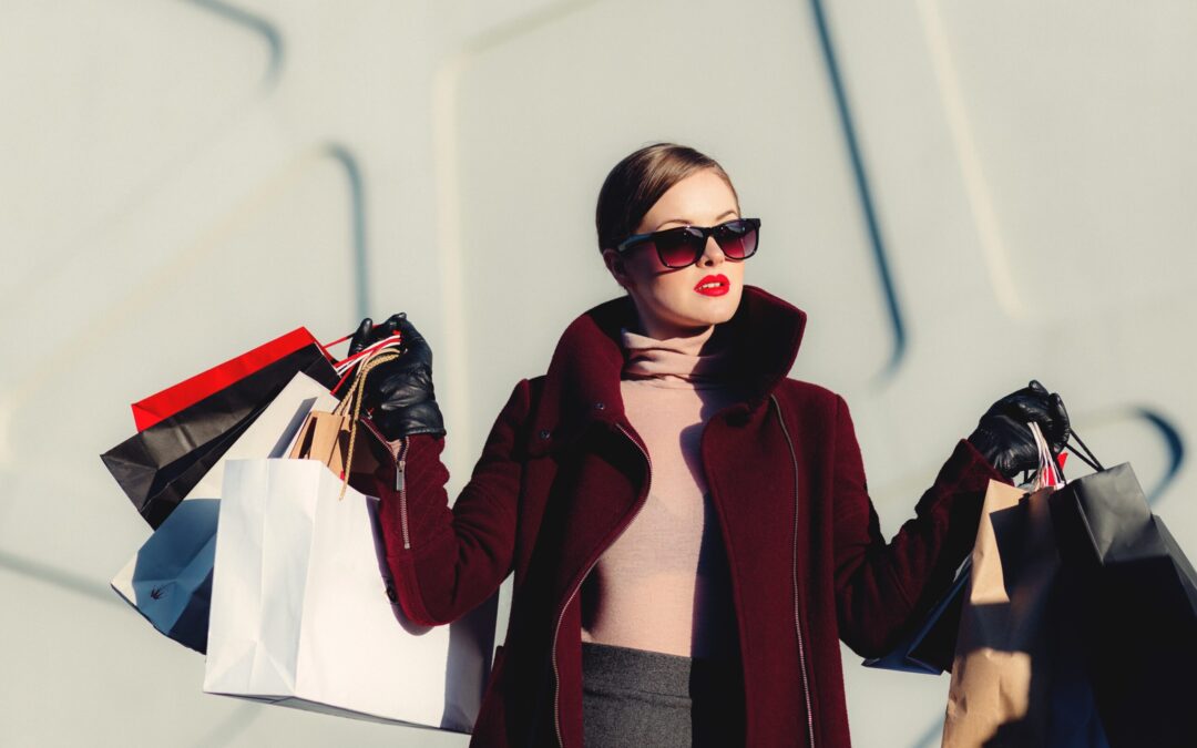 a woman holding 4 bags of differnt colors in each hand who is richly dressed wearing very red lipstick and sunglasses. Shopping spree!