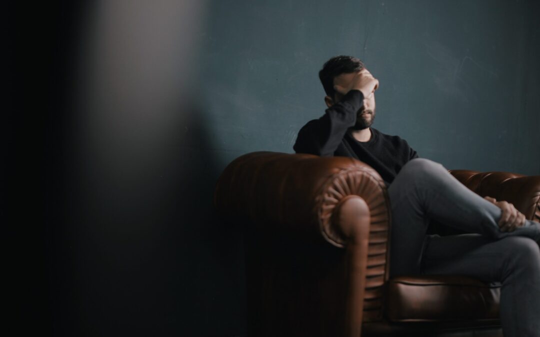 A man holding his forehead with his right hand sitting on a sofa