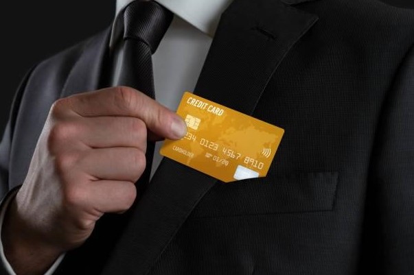 a man in a suit is pulling out a gold credit card out of his lapel pocket.